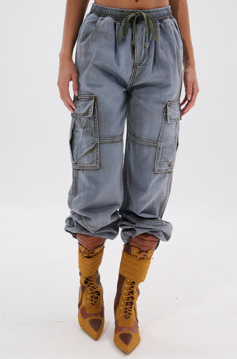 Someone wears the WALLEY CARGO JOGGER in light blue, featuring a high-rise fit, oversized cargo pockets, drawstring waist, and cuffed ankles, paired with yellow lace-up heeled boots with cutout details. 1