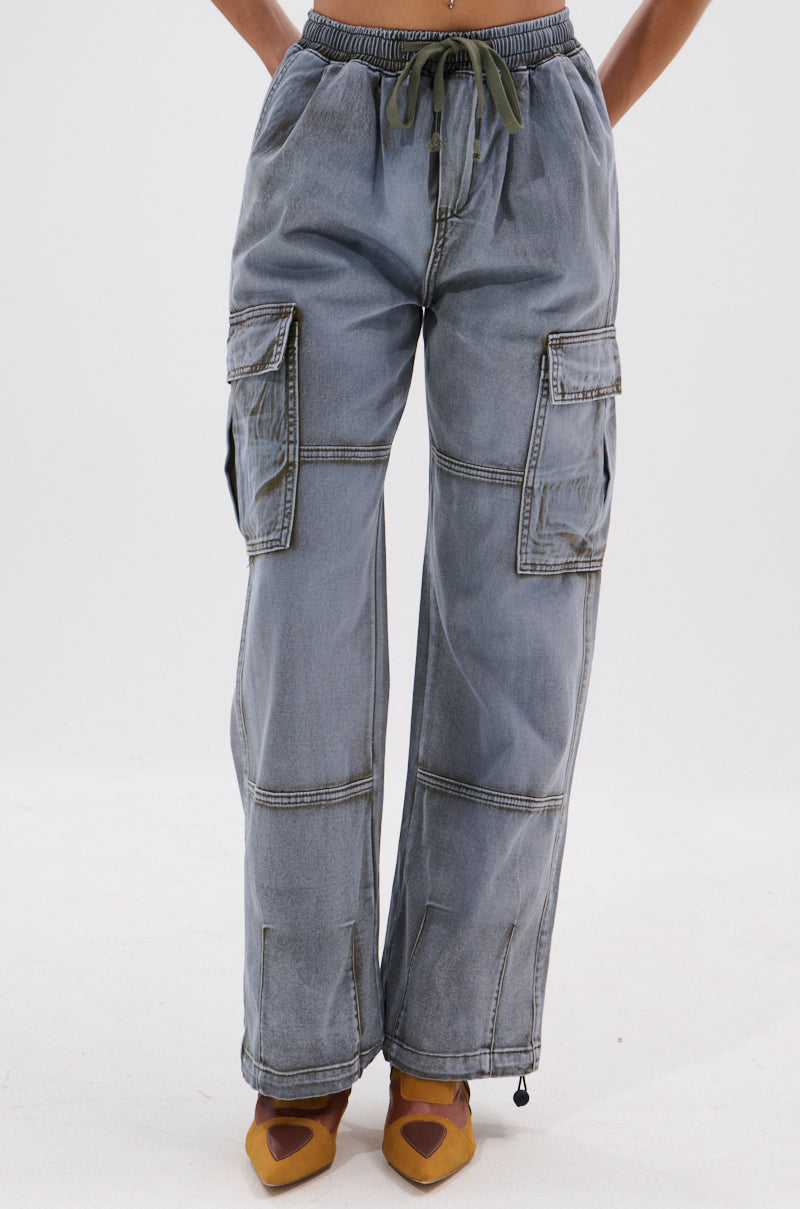A person wears the WALLEY CARGO JOGGER—loose-fitting, light-wash pants with large side pockets, drawstring waist, and visible stitching—paired with mustard yellow pointed-toe shoes against a plain white background. 2