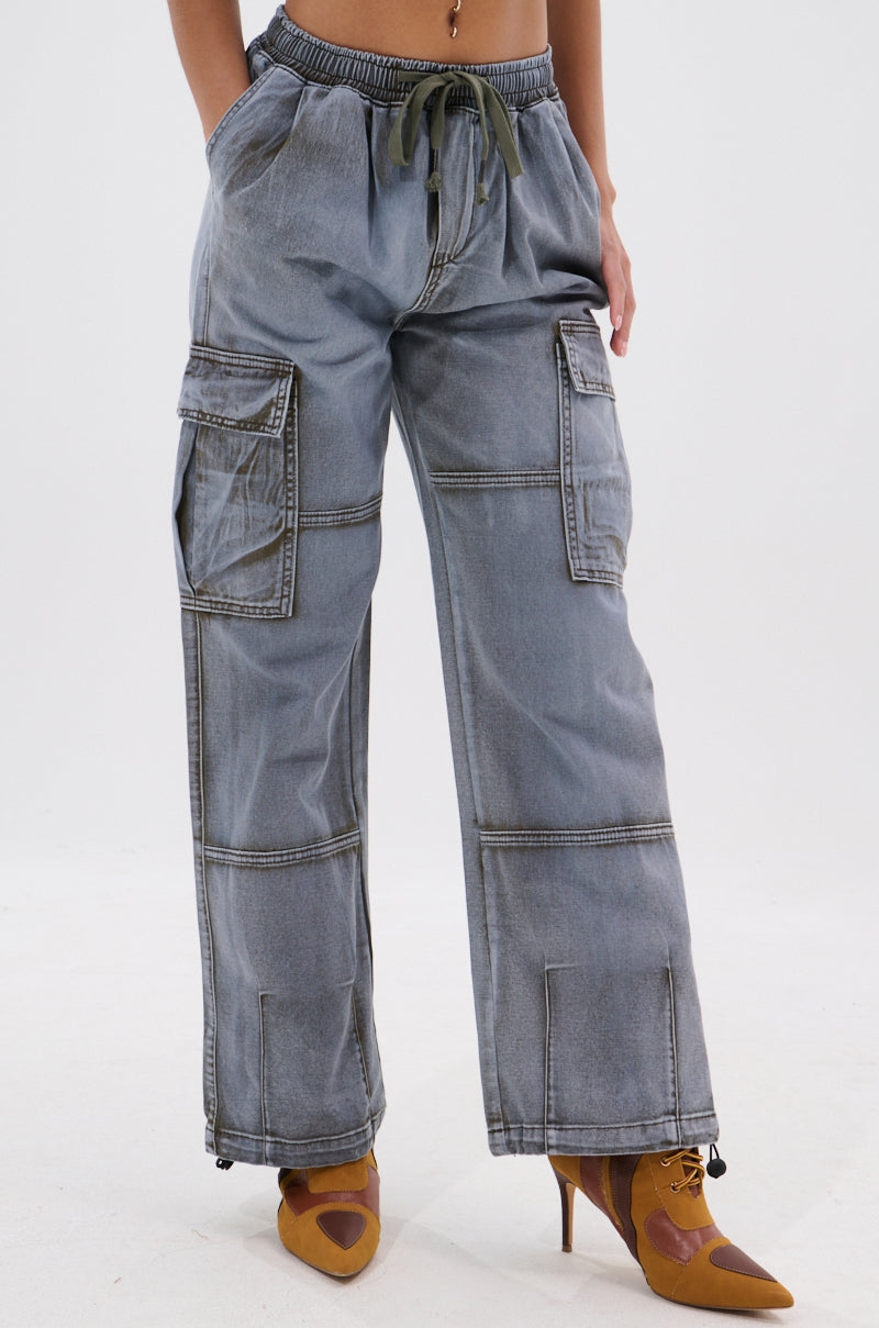 A person models the WALLEY CARGO JOGGER—high-rise, light-wash jeans with oversized cargo pockets and drawstrings—styled with tan pointed-toe heels against a plain white background. 3