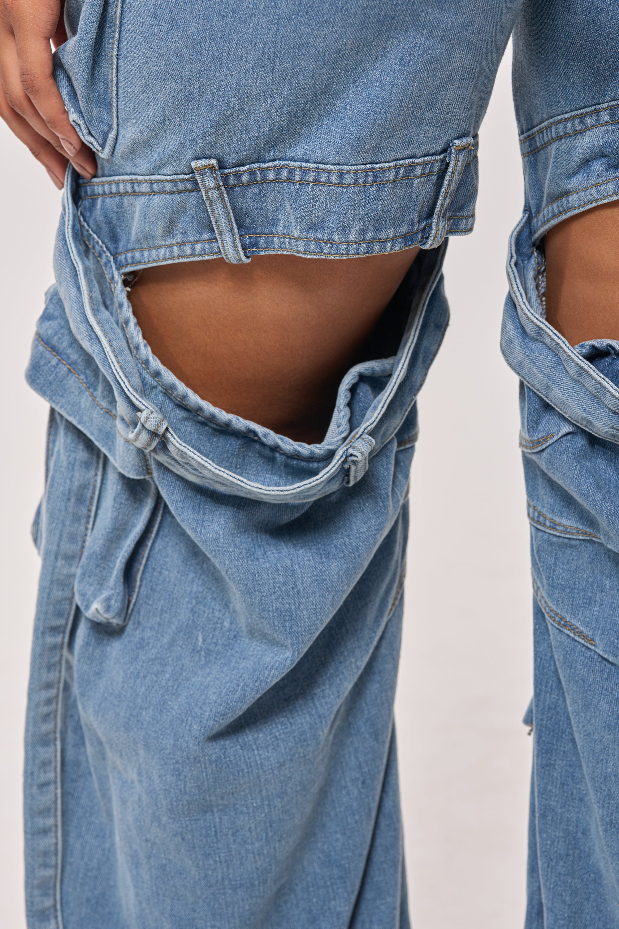 A close-up of a person wearing CHECK OUT THE BACK CUTOUT RELAXED DENIM with large horizontal thigh cutouts, revealing skin beneath. These loose-fitting jeans feature a wide-leg silhouette and a unique distressed look. 8