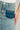 Close-up photo of the waist and pocket area of a light blue, TOO GOOD FOR YOU DENIM MIDI SKIRT featuring high-rise design with a contrasting dark blue pocket. A woman's hand rests on her hip as she wears a white top tucked into the curve-hugging skirt, which has slightly distressed fabric.