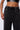 A person wearing the BRIGHT LIGHTS BIGGER CITY JOGGER, which features high-waisted, dark gray, mineral wash sweatpants with an elastic waistband and drawstring. They pair the jogger pants with a shiny black crop top adorned with rhinestone detailing, revealing a portion of their midriff.