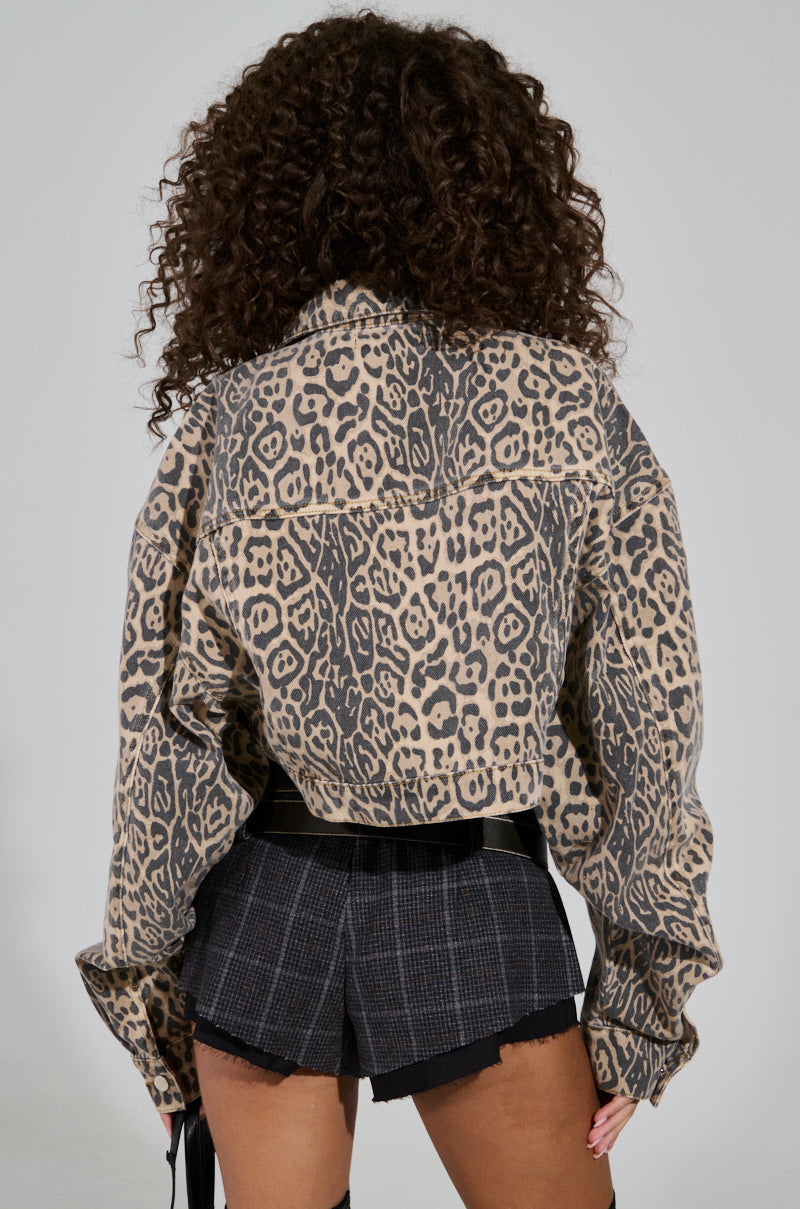 Rear view of a person with curly hair wearing the NO CHEATING PRINTED DENIM JACKET, which features a leopard print pattern, paired with plaid shorts. They stand confidently against a plain background.