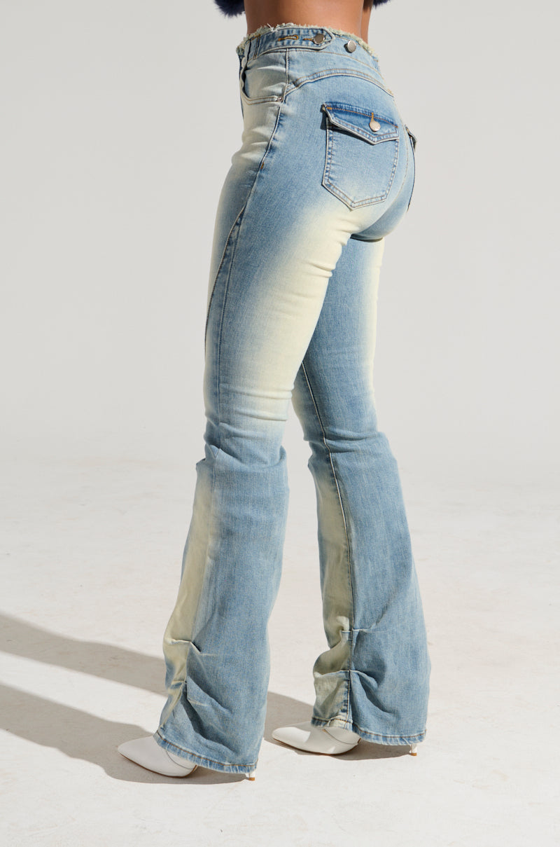 A person is wearing the "Washed Up For Good Denim Pant" - high-rise, light-wash jeans with a subtle flare at the bottom. These super stretchy pants feature a back pocket adorned with a button. The individual stands against a white background, complementing the look with white, pointed-toe heels.
