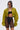 She wears the TAKE IT EASY CROPPED BOMBER IN GREEN over a black crop top and sheer black high-waisted shorts, accessorized with sunglasses, a chain necklace, and two ponytails, standing against a light background.