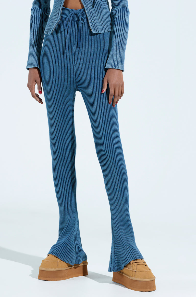 Someone is modeling the HOT GIRL FLARED LEGGING in stretchy knit blue with a high-rise drawstring waist and flared legs, paired with tan platform shoes against a calming light pastel blue background.
