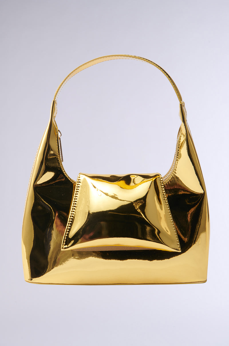 The IN LONDON WITH IT PURSE is a shiny, metallic gold handbag with a structured shape, single handle, and front pocket, photographed against a plain light gray background.