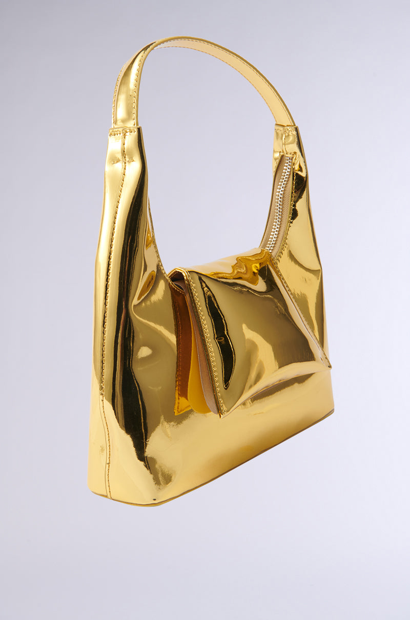 The IN LONDON WITH IT PURSE is a shiny gold structured shoulder bag featuring a wide strap, angular silhouette, and prominent zipper, showcased against a plain light gray background.