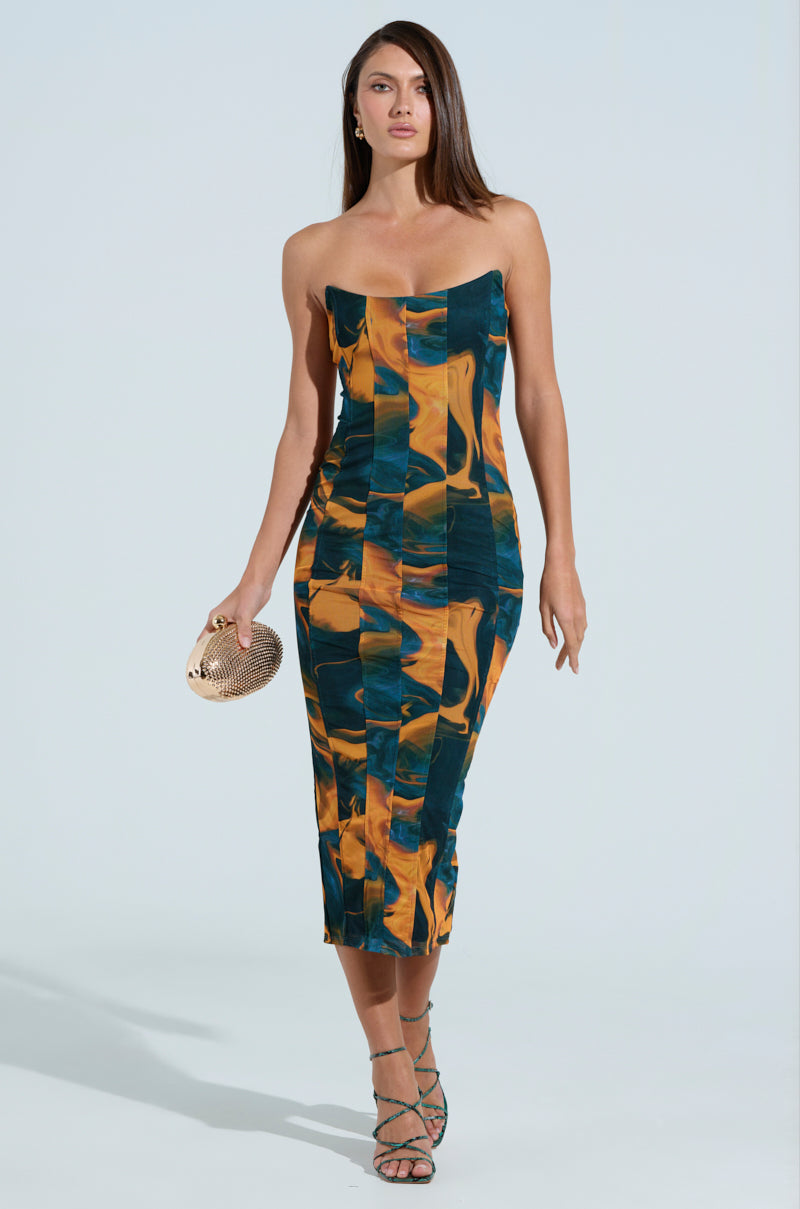 A woman confidently walks in a bodycon SHES UNFORGETTABLE ABSTRACT MESH MIDI DRESS with a strapless neckline. She clutches a small textured purse in her right hand and dons strappy sandals, all set against a light, plain background.
