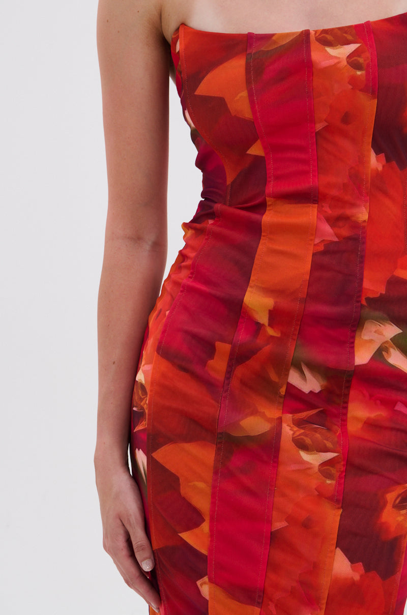 A close-up of a person in the ARCHETYPE PRINTED MIDI DRESS, showcasing its vibrant red and orange abstract floral print and bodycon silhouette, with their left arm relaxed at their side. 5