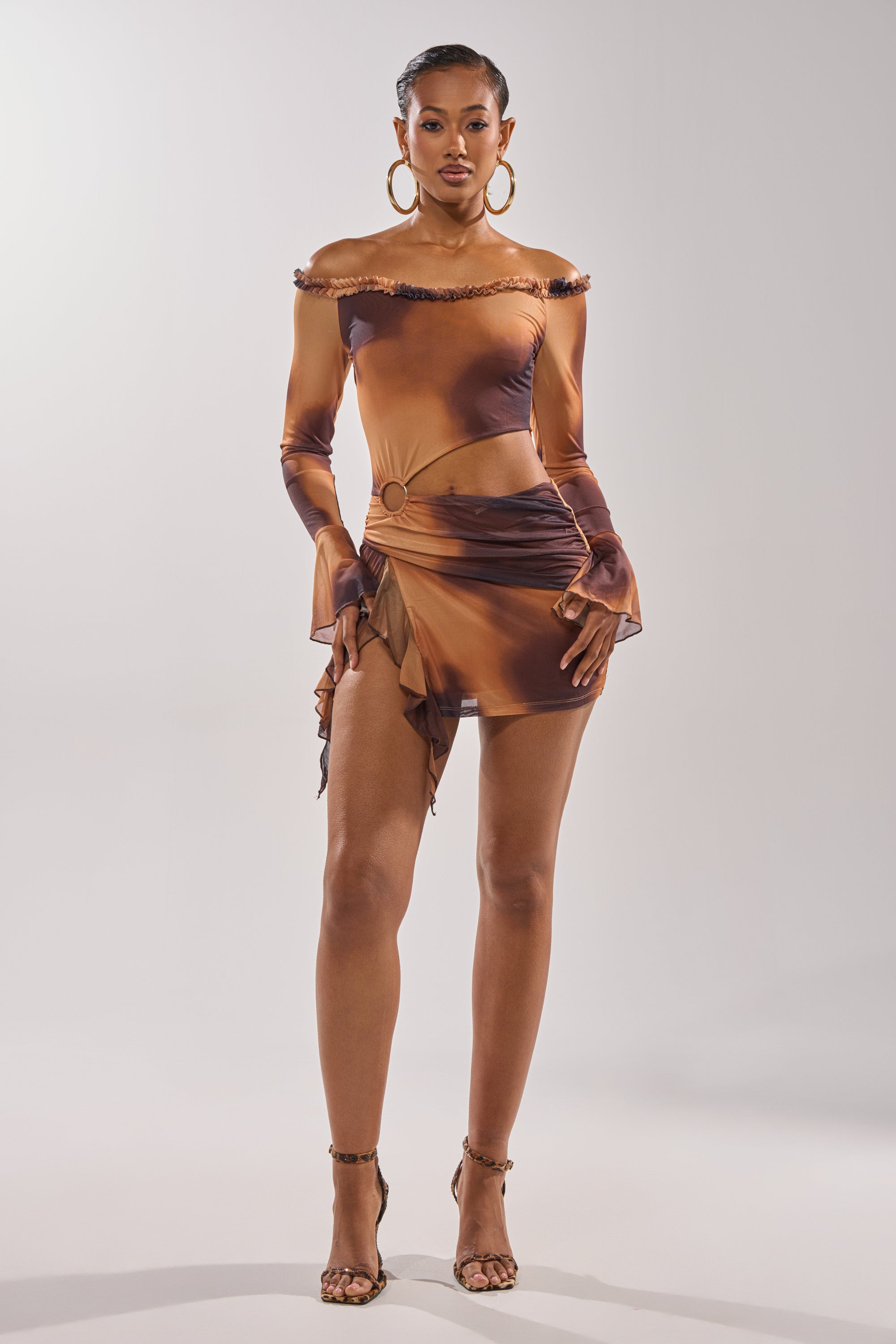 A woman stands confidently in the GIVE IT TO ME BABY MINI DRESS, a fitted off-shoulder mesh mini with brown and orange ombre, side cutout, ruffled hem—styled with hoop earrings and heels—perfect for making a statement at any party. 5