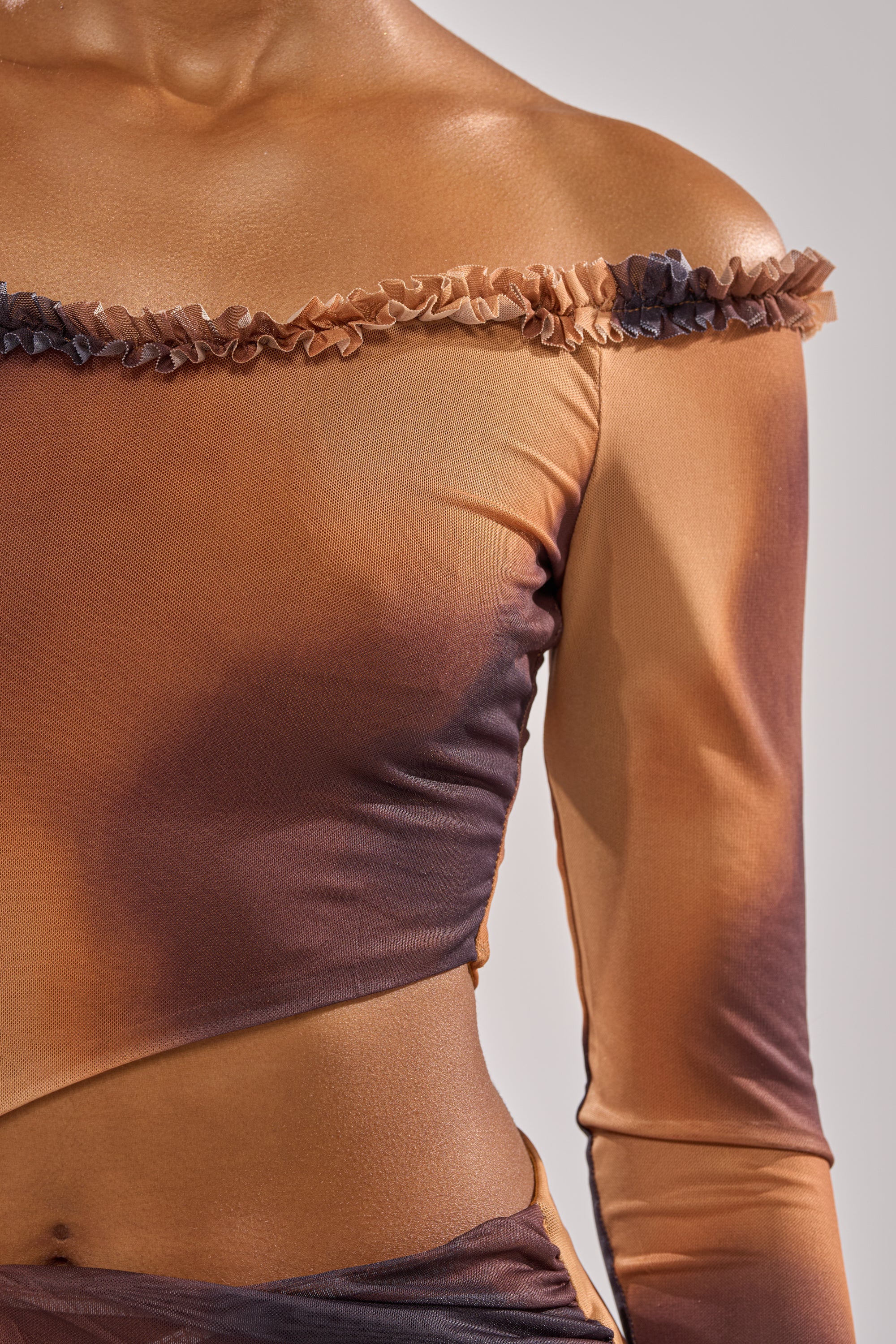 A close-up of a person wearing the GIVE IT TO ME BABY MINI DRESS, an off-shoulder mesh dress in brown and orange with long sheer sleeves and a ruffled neckline. Only the upper torso and part of the arm are shown. 6
