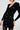 A woman models the SUSIE MINI DRESS IN BLACK, featuring a fitted design with embossed gold buttons. One hand rests by her side while the other is slightly bent. This bodycon silhouette showcases a deep V-neck and structured detailing for an elegant and contemporary appearance.