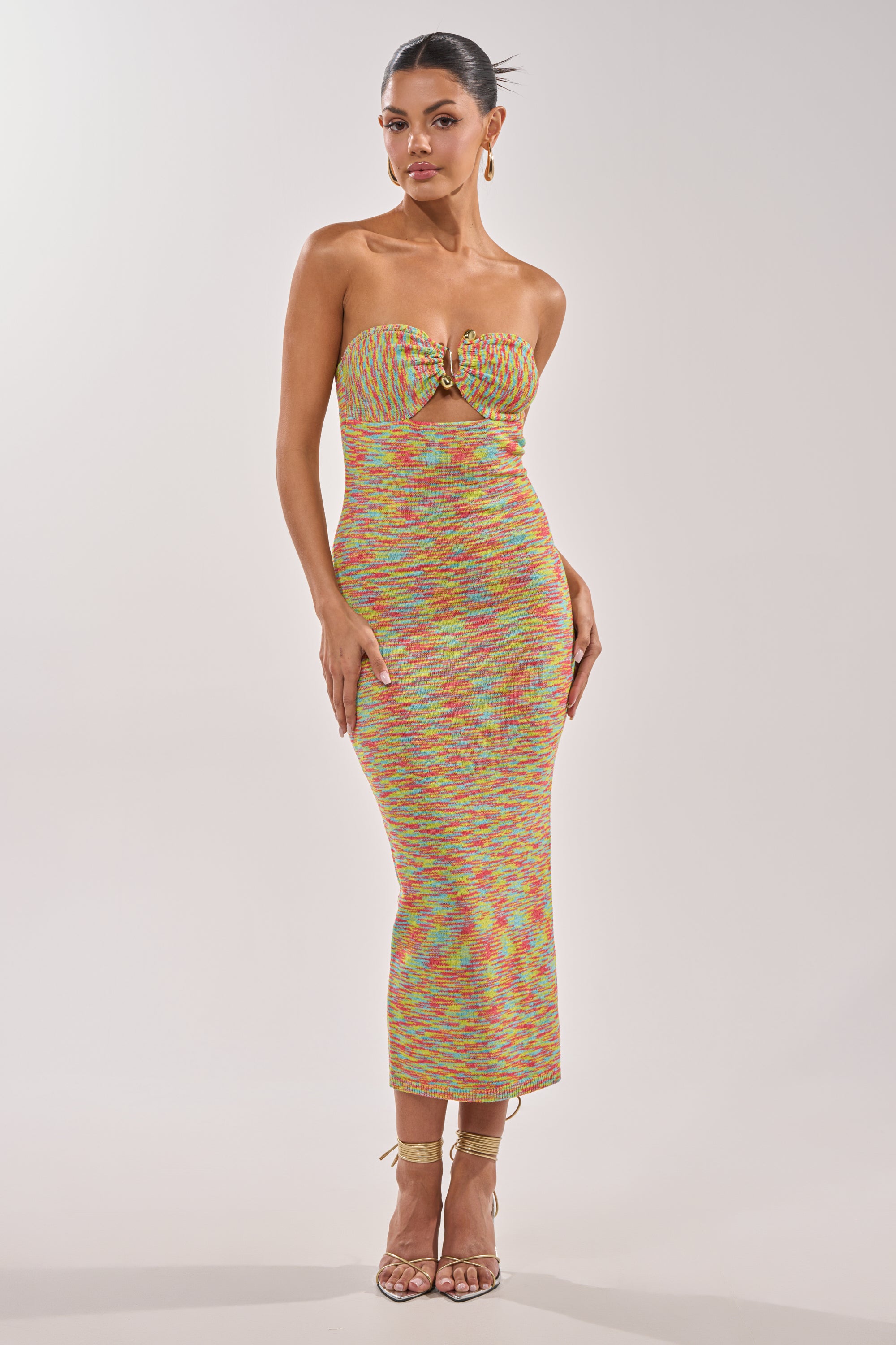 A woman poses confidently in the STARRY NIGHT KNIT MIDI DRESS IN MULTI, featuring a multicolor textured knit and strapless midi silhouette. She completes her look with slicked-back hair, hoop earrings, and strappy heels against a plain background. 0