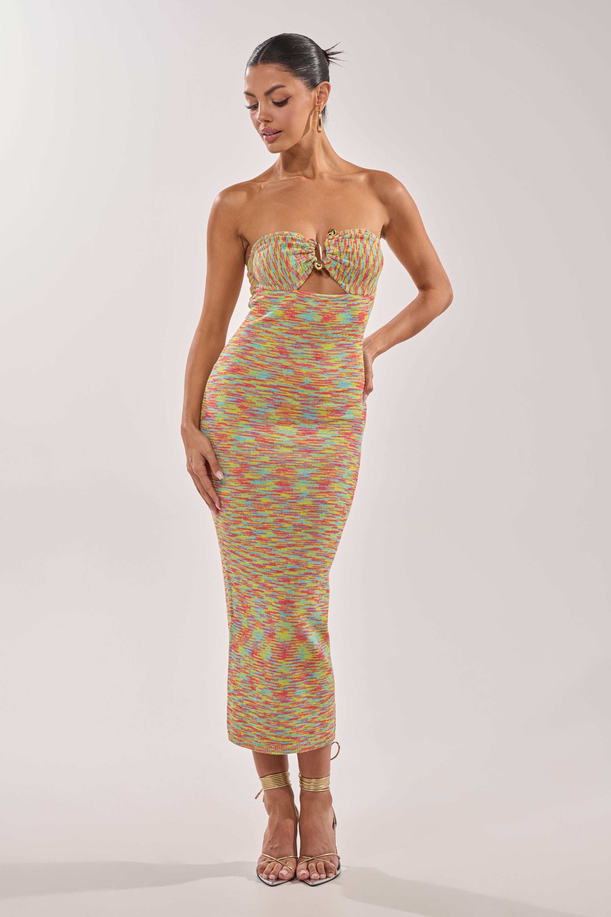 A woman models the STARRY NIGHT KNIT MIDI DRESS IN MULTI—a strapless, multicolor knit midi dress with a front twist and gold hardware—paired with strappy high-heeled sandals against a plain light background. 1