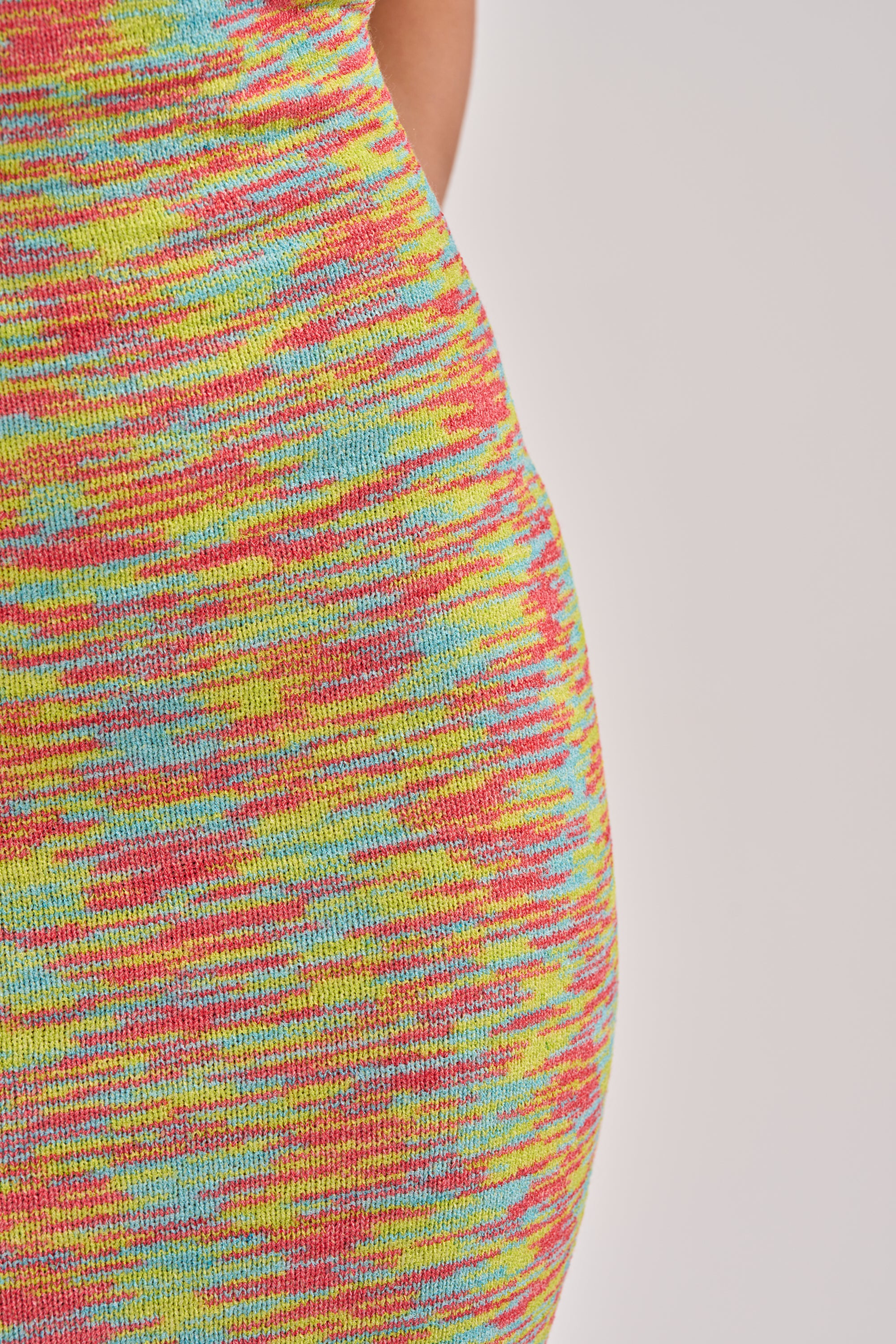 Close-up of the STARRY NIGHT KNIT MIDI DRESS IN MULTI, a fitted midi dress with body-contouring silhouette and a vibrant multicolored knit pattern in yellow, red, blue, and pink against a plain light background. 5