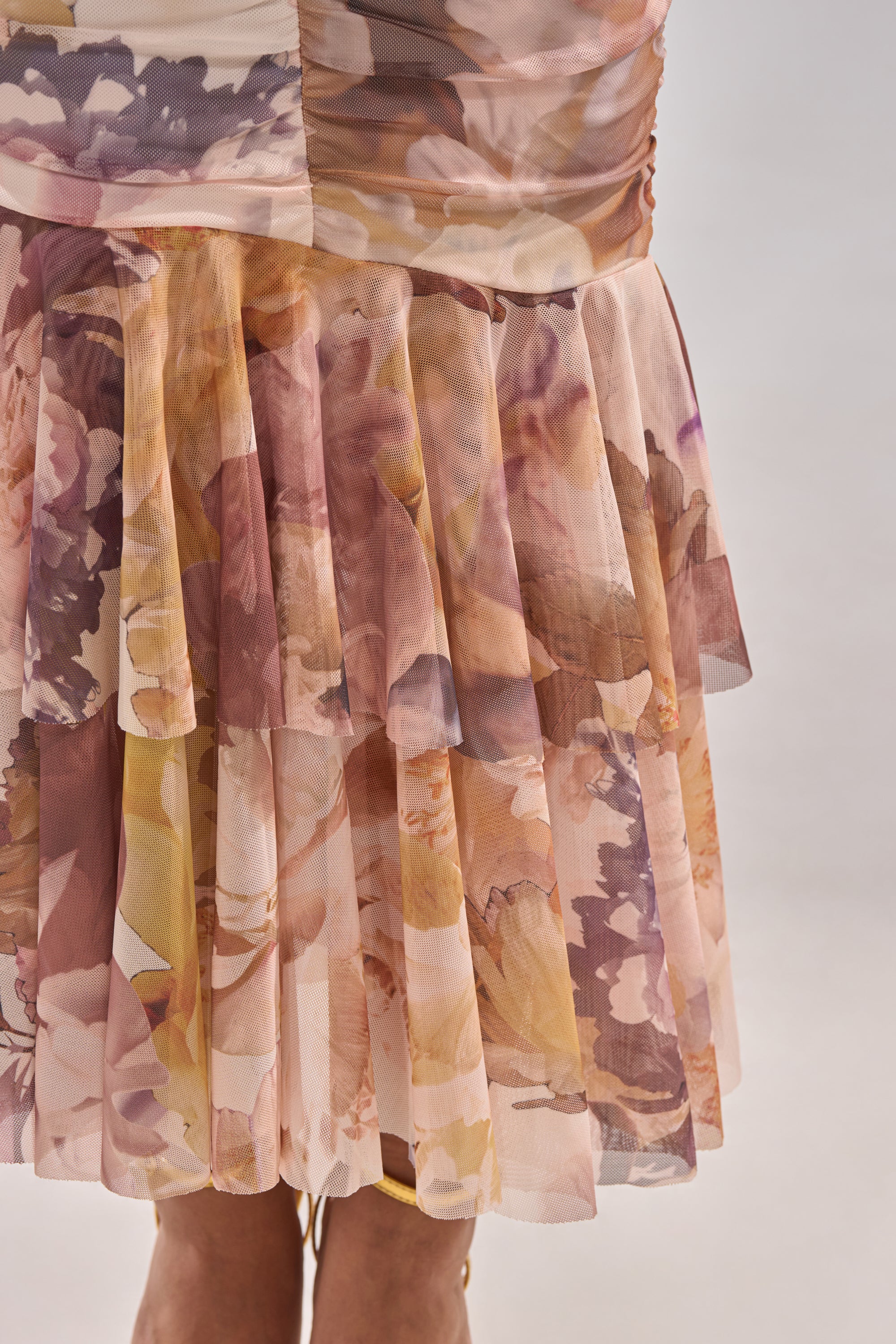 Close-up of the LOVER GIRL SLINKY MIDI DRESS, showcasing its sheer, pleated skirt with soft pink, purple, yellow, and beige floral patterns. The image highlights the dress’s delicate texture and elegant design.