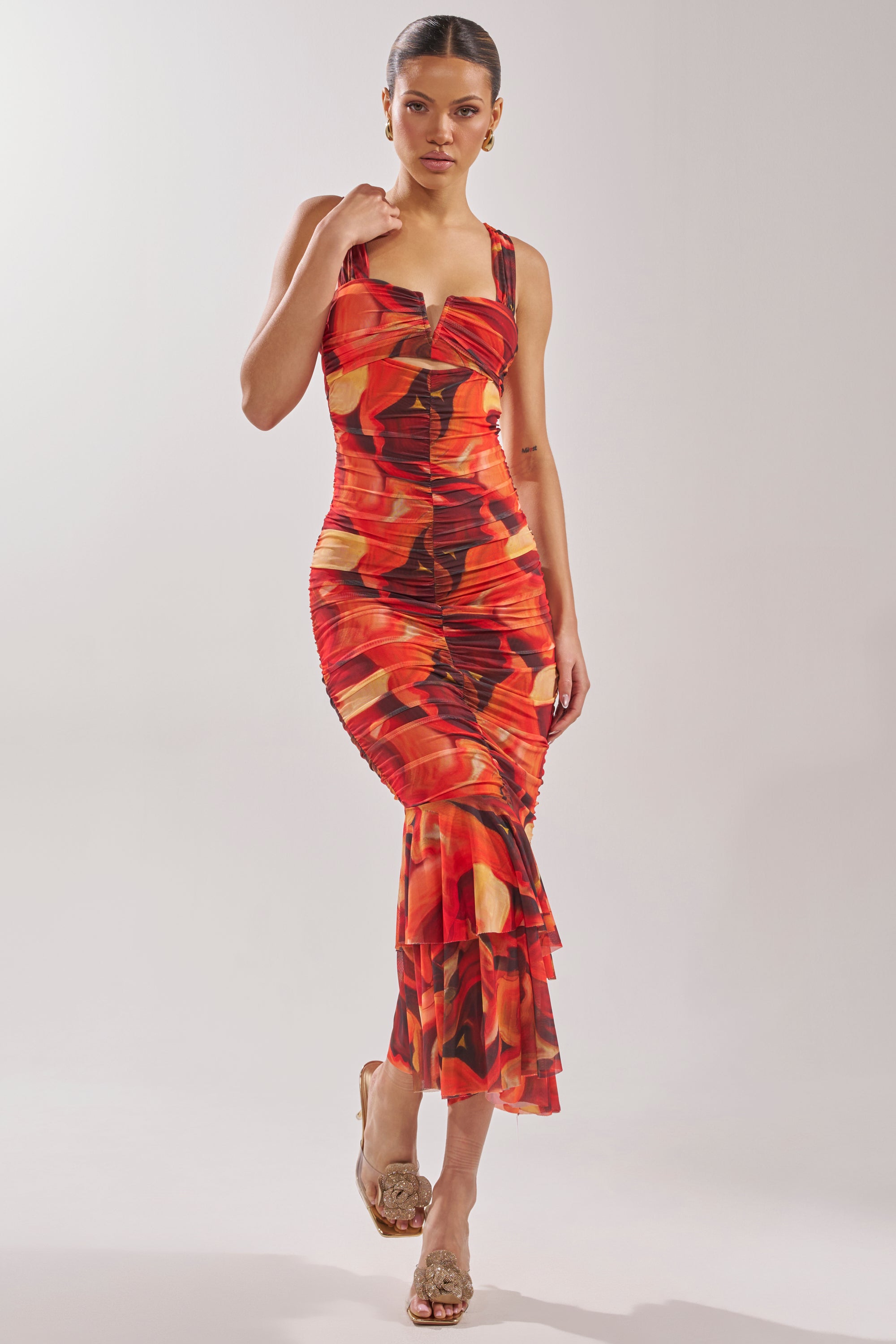 A woman models the BELONG IN A MUSEUM RED MAXI DRESS, featuring a bold red, orange, and black abstract flame print, styled with hoop earrings and open-toed sandals against a simple light background. 0