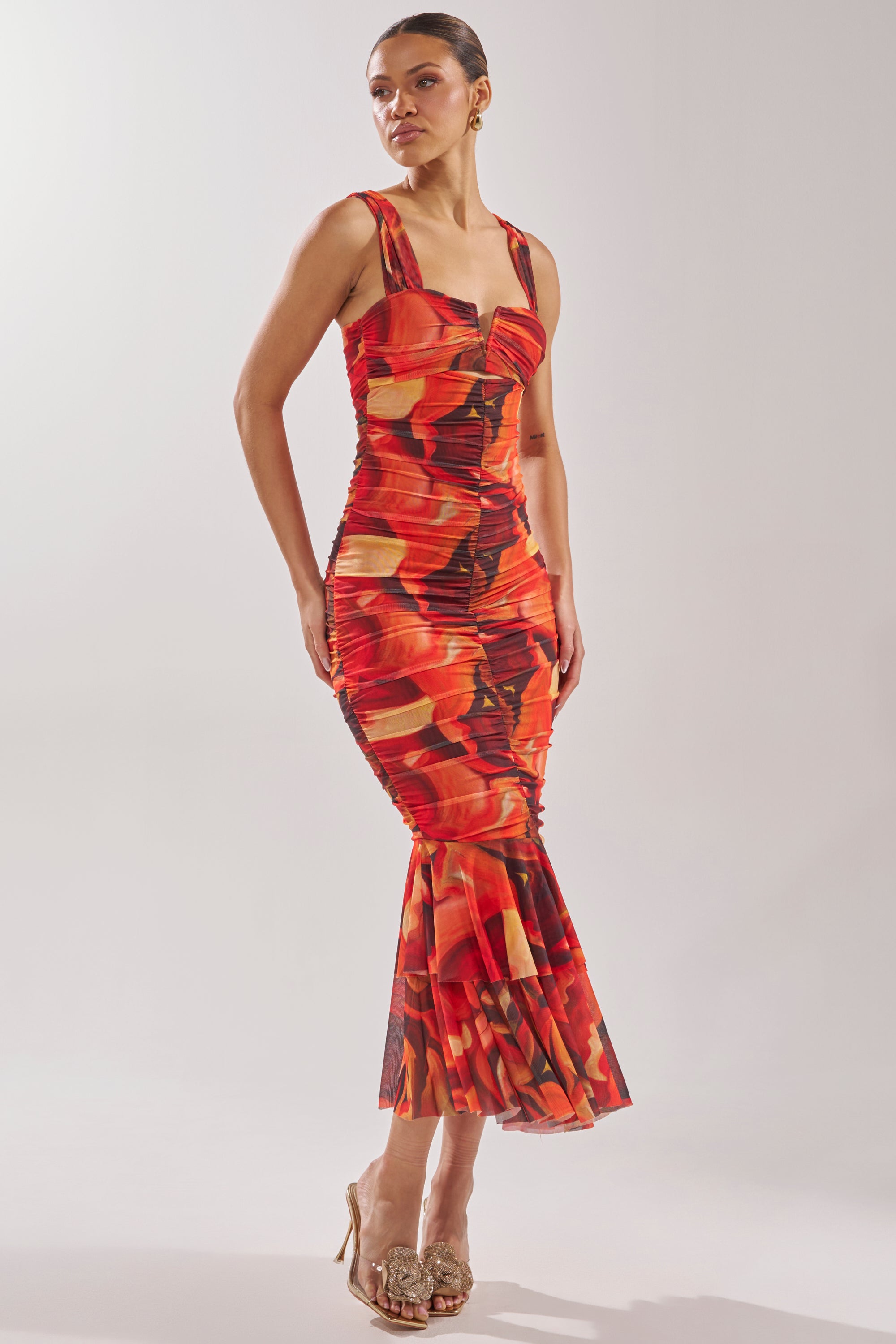 A woman wears the BELONG IN A MUSEUM RED MAXI DRESS, a fitted sleeveless dress with a flared hem, styled with beige heeled sandals. Her hair is tied back as she poses against a plain light background. 3