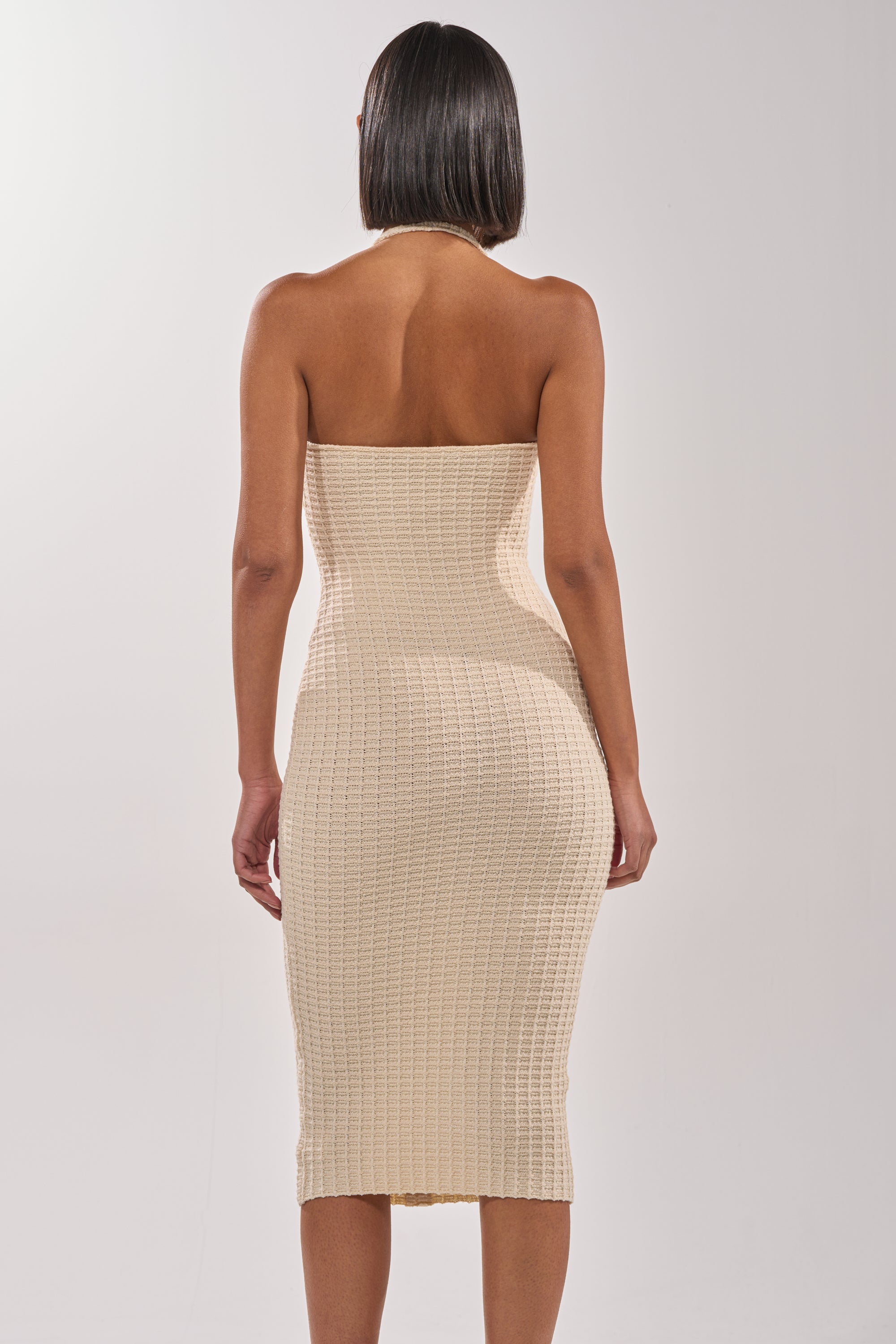 A woman with short, straight hair is seen from the back wearing the BUTTONED DOWN BADDIE MIDI DRESS IN WHITE, featuring an ivory textured fabric and a form-fitting silhouette against a plain white background. 3