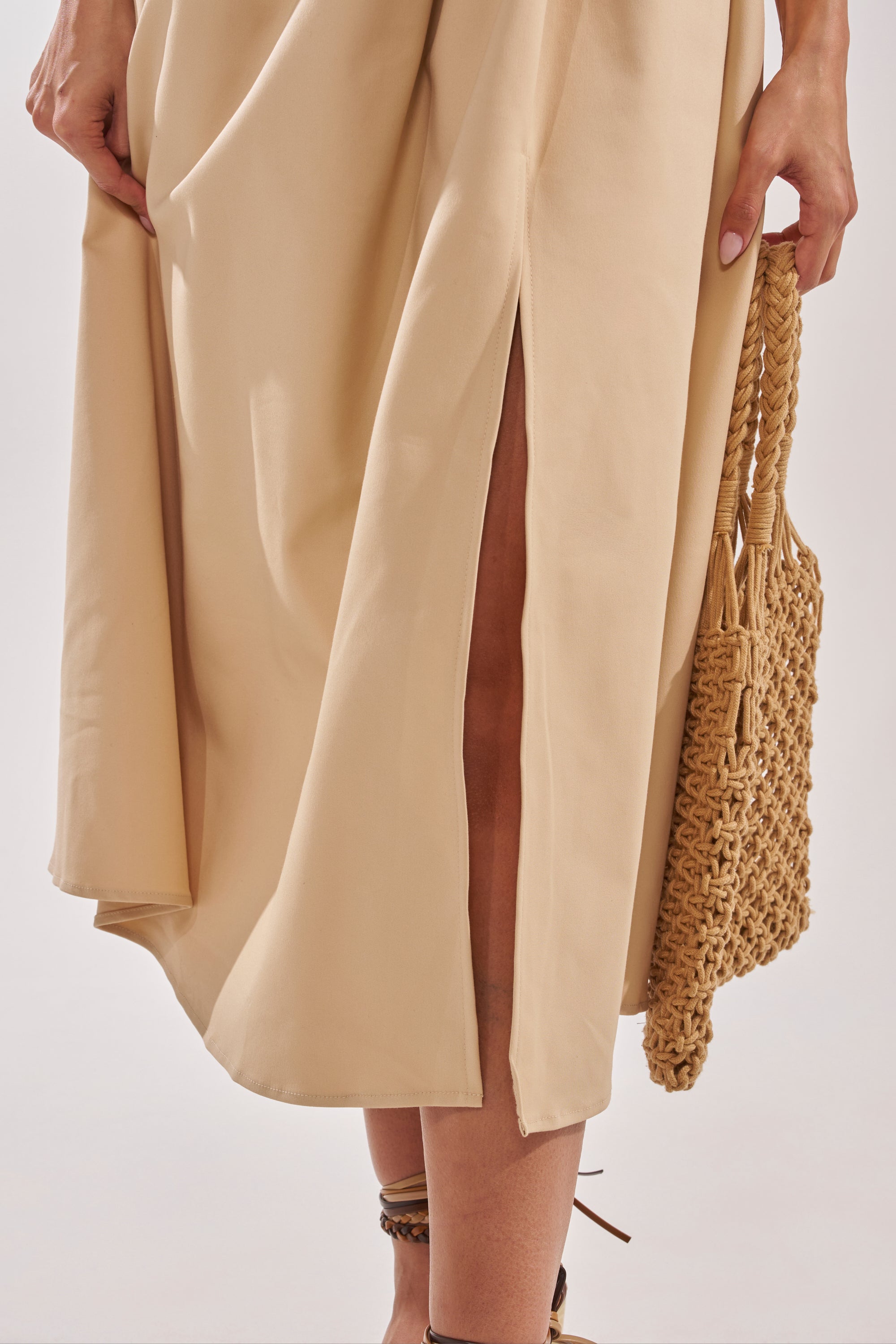 A person in the SWEET SOFIE HALTER MIDI DRESS with a high slit, holding a woven straw handbag. Only the lower part of the dress and their hand are visible. 7