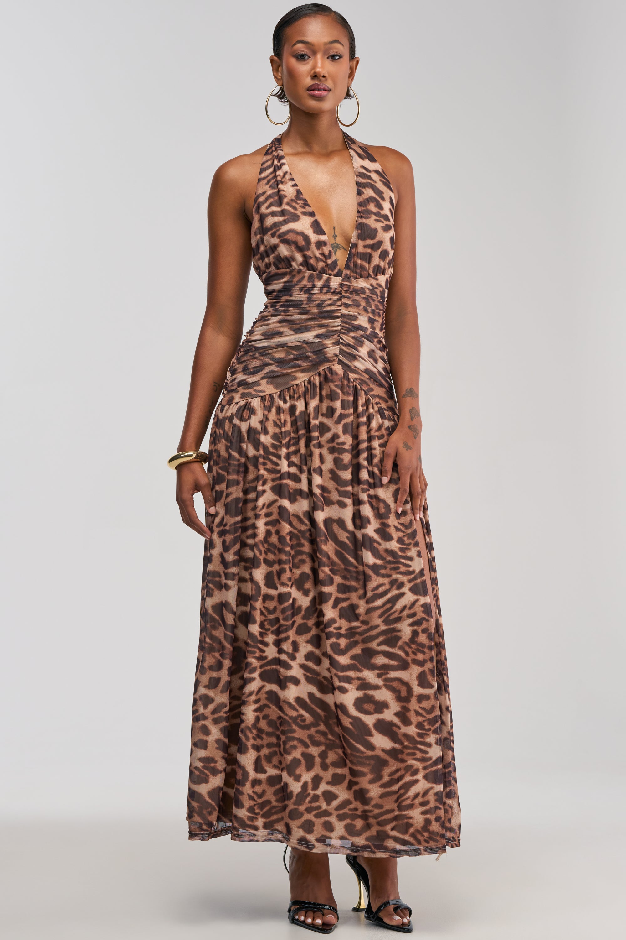 A woman wearing the SUGAR RUSH Mesh Maxi Dress in Animal, a sleeveless halter dress featuring a striking brown and black cheetah print, stands against a plain light background.
