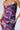 A person wearing the FLORAL FANTASY RUCHED MIDI DRESS, featuring a strapless design with a bodycon fit, showcases vibrant abstract floral patterns in shades of purple, pink, and teal. Ruching along the sides and front adds texture while their hands gently rest on their hips.