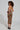 A person with curly hair models the Ziggy Midi Dress in Orange, a sleeveless and backless piece featuring an Art Deco print in orange, black, and beige. Posed sideways in black heels, they highlight the dress's curve-hugging silhouette while gazing into the camera.