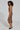 A person with curly hair poses in the ZIGGY MIDI DRESS IN ORANGE, which features a colorful pattern of orange, black, and tan swirls. They showcase the dress's curve-hugging silhouette while standing sideways in black heeled sandals against a simple light background.