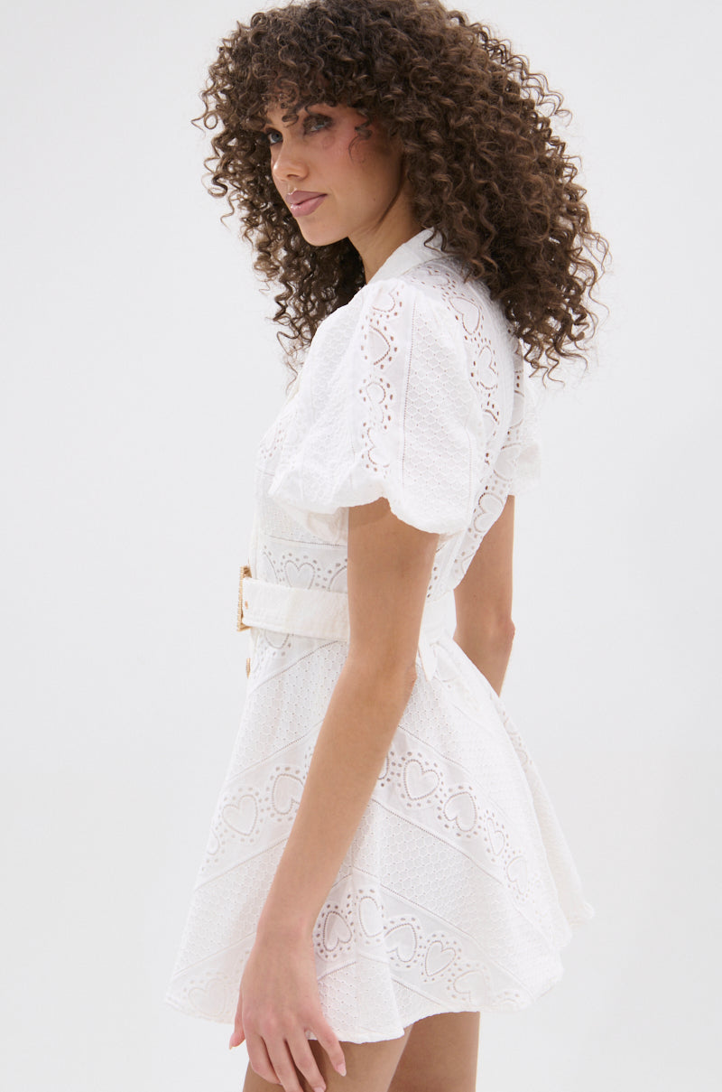 A woman with curly hair models the TRUE DELIGHT BELTED MINI DRESS, a fit and flare mini dress with puff sleeves and eyelet details, shown in a side pose against a plain light background. 3