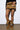 A person wearing a faux fur mini skirt with an abstract pattern and matching ADA LEOPARD FLAT BOOTIE, which features a leopard print design. They are standing against a plain white wall with a visible floor surface.