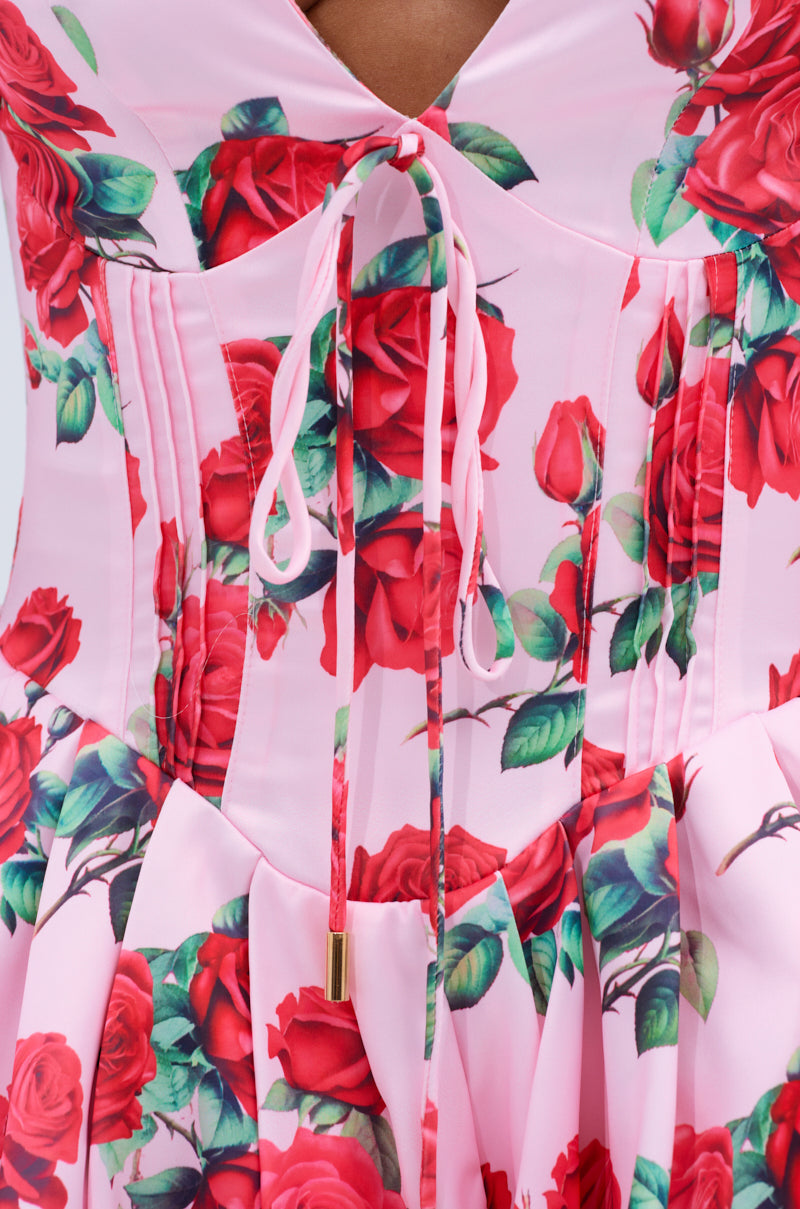 Close-up of the WILL YOU TAKE THIS ROSE SATIN MINI DRESS—a pink mini with a fitted corset-style bodice, red and green rose prints, vertical seams, puff sleeves, and a central bow tied with pink strings.