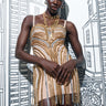A model poses in front of a backdrop with sketched buildings, highlighting the GOLDEN GIRL CHAINED UP MINI DRESS. This bodycon design boasts faux gold and silver metallic chain links along with multiple layered necklaces, offering a chic and artistic look.