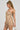 Wearing the GOLDEN GIRL CHAINED UP MINI DRESS, a woman displays a bodycon silhouette accentuated by faux gold and silver metallic chains. In profile, her long braided hair is tied back as she carries a matching handbag. Her shoulder and arm are adorned with tattoos, completing her striking ensemble.