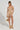 A woman stands confidently in the GOLDEN GIRL CHAINED UP MINI DRESS, sparkling in its faux gold and silver metallic chains. She carries a spherical gold purse, complemented by matching sandals. Her braided hair is neatly styled, and her arm tattoos enhance the dress's bodycon silhouette.