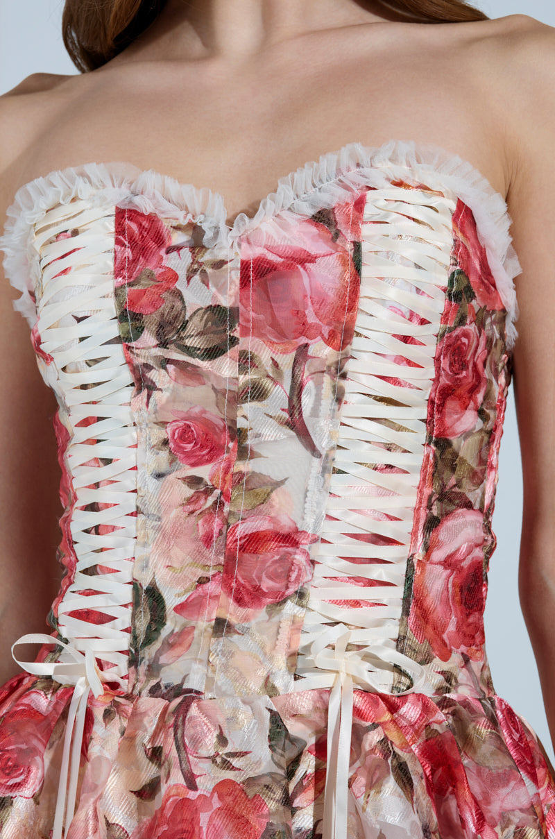 The KEEP DREAMIN FLORAL MINI DRESS features a strapless silhouette adorned with pink and red roses, vertical ribbon lacing on the bodice, and ruffled trim along the top. Its sheer overlay adds romantic charm to this enchanting floral mini dress.