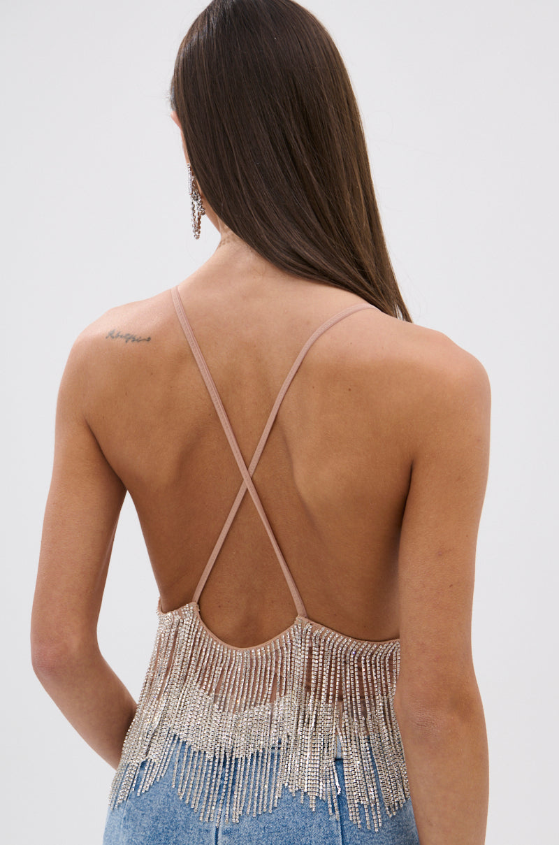 A woman with long brown hair is seen from the back wearing the SHINING STAR RHINESTONE FRINGE TANK TOP featuring beaded rhinestone fringe, thin crisscross straps, and light blue jeans, with a small tattoo on her upper right shoulder.