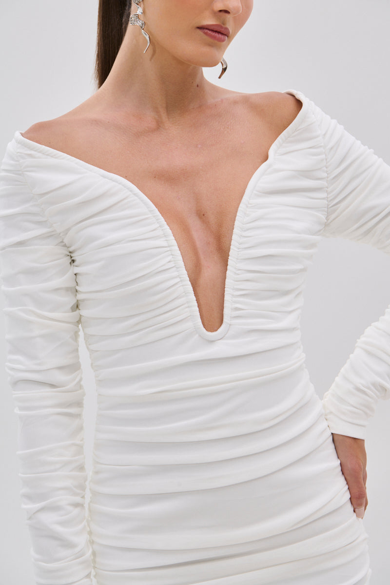 Woman wearing the TARAJI Bandage Midi Dress with Mesh Overlay, featuring a white long-sleeve design, off-the-shoulder deep V-neckline. She accessorizes with statement earrings and has her hand on her hip.
