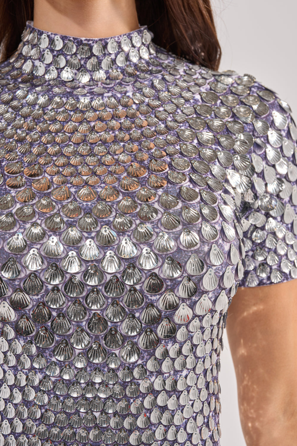 Close-up of the FAR FROM BASIC SEQUIN MINI DRESS IN SILVER, featuring a high collar, short sleeves, and overlapping shell-shaped sequins for a textured, reflective look—ideal for summer parties. 6
