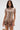 A woman stands against a plain background wearing the FAR FROM BASIC SEQUIN MINI DRESS, a shiny, metallic rose gold mini dress with short sleeves and a high neckline, holding a small round gold handbag embellished with shell accents.