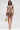 A woman wears the FAR FROM BASIC SEQUIN MINI DRESS, a shiny rose gold mini with short sleeves and a flared hem. She holds a gold fringe bag and wears matching rose gold shoes, standing against a white background.