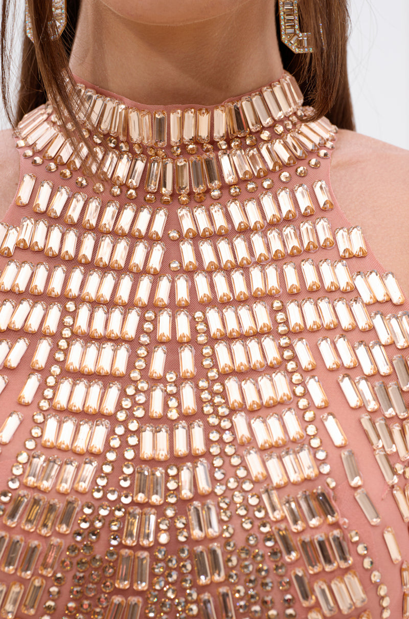 Close-up of a woman's neck and upper chest wearing the SHINE BRIGHT RHINESTONE MESH MINI DRESS IN ROSE GOLD, featuring a high neckline adorned with rows of reflective, rectangular gold beads and matching earrings.