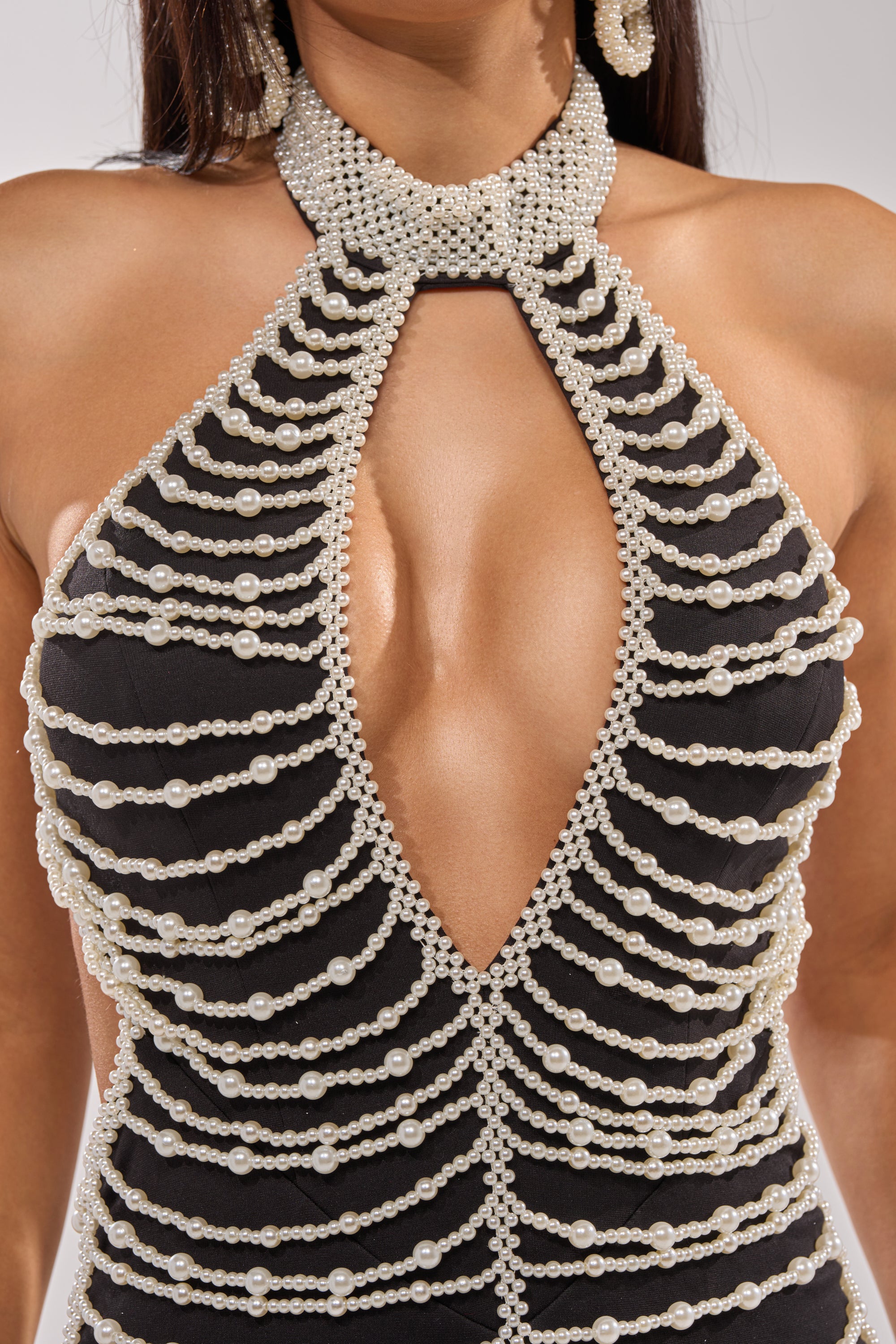 A close-up of a woman wearing the ELECTRIC DIAMOND ROMPER, a black halter-neck romper with rows of white pearls, a deep V neckline, and a keyhole chest cutout—ideal for chic evening occasions. 12