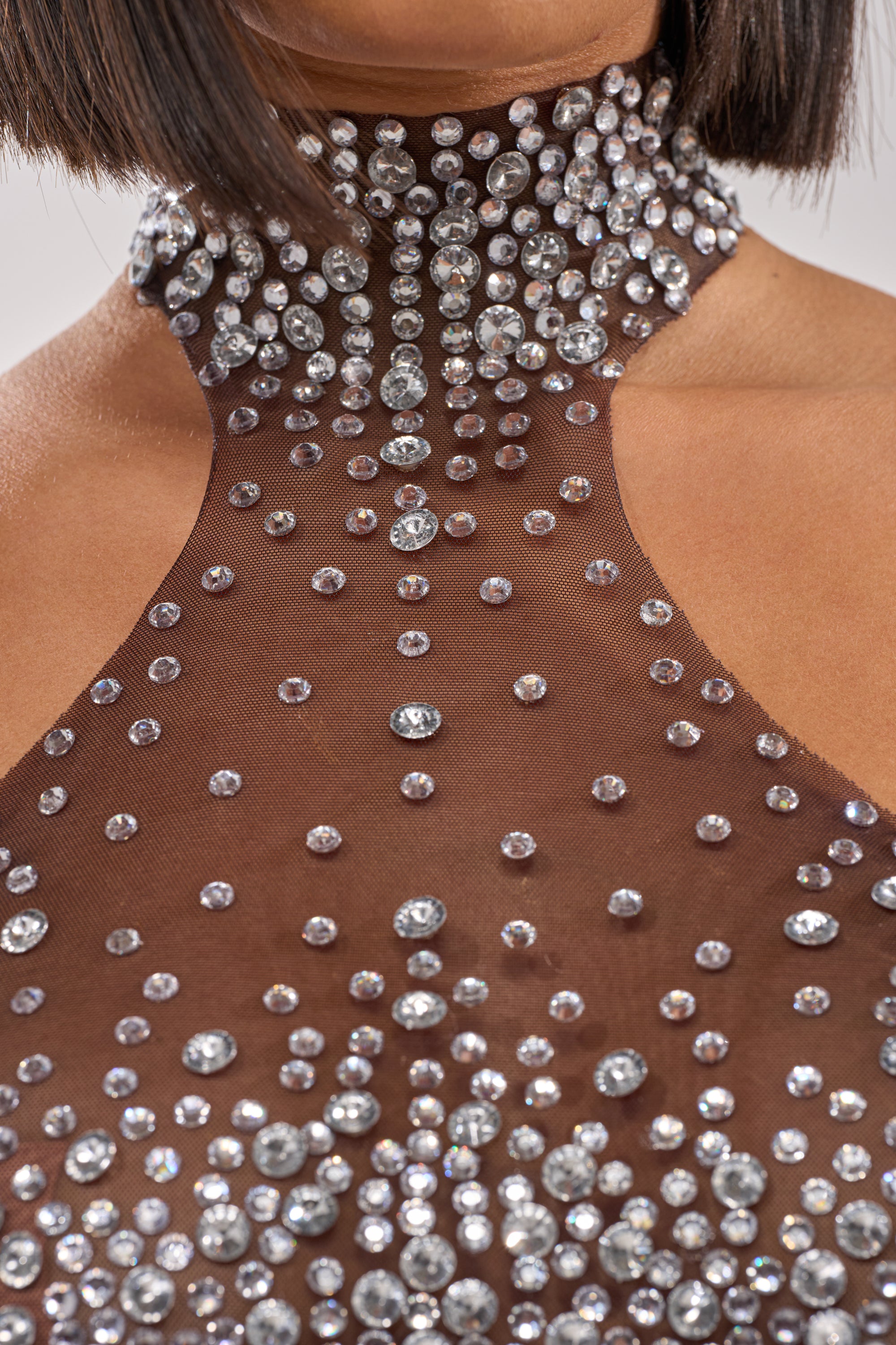A close-up of a person in the ALL YEAR ROUND SHEER RHINESTONE TOP, featuring a sheer brown halter style and high neckline. The rhinestones sparkle, complementing the chic look of their short, straight bob haircut. 6