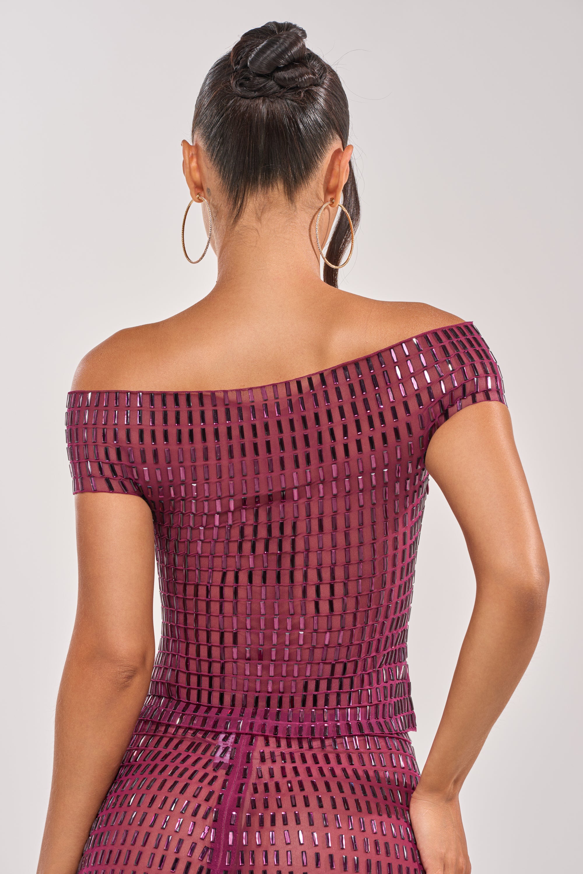 A woman with hoop earrings and an intricate updo is seen from the back, wearing the SHAKE IT FOR ME BABY RHINESTONE TOP—an off-the-shoulder maroon party top with a shiny square grid pattern. 7