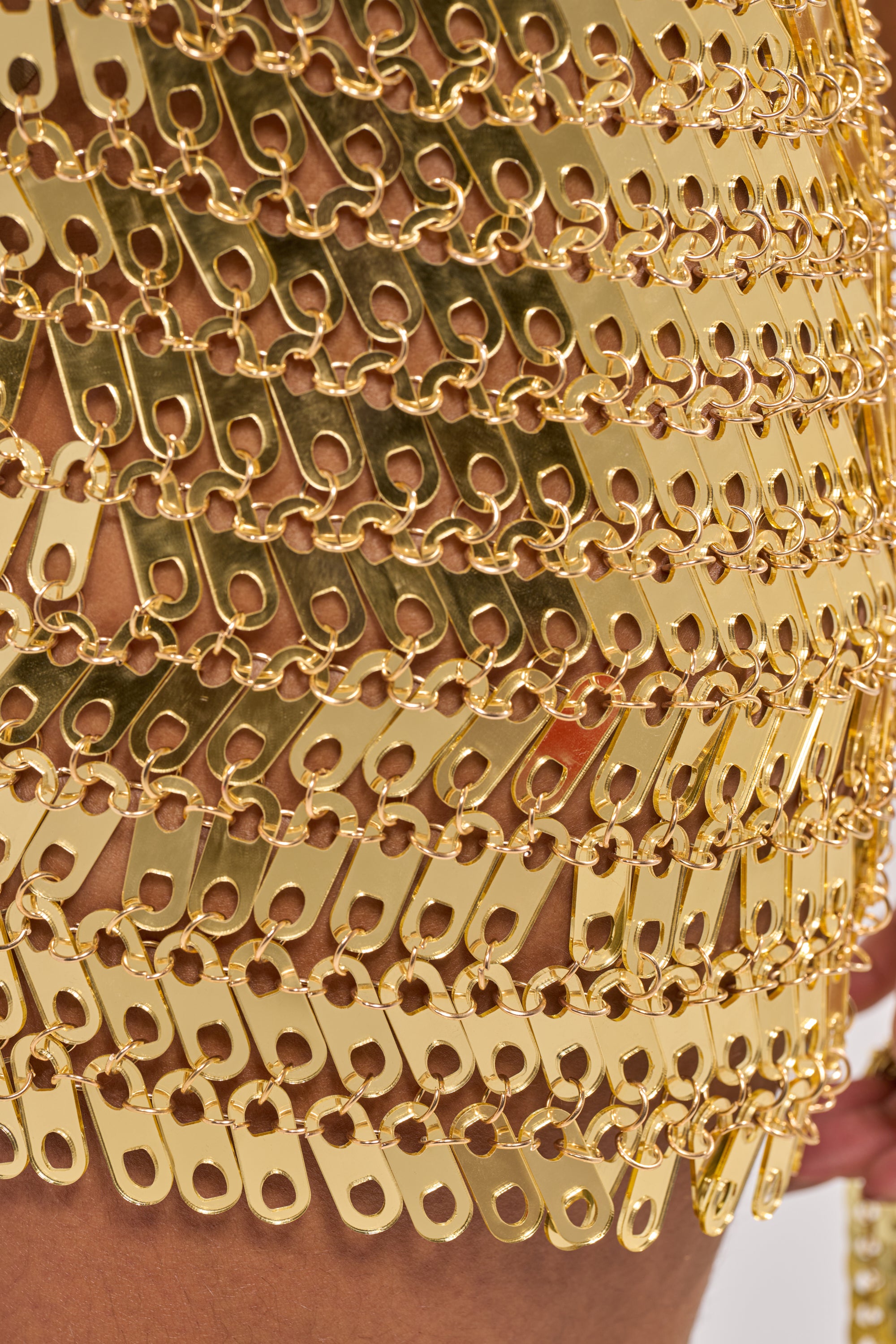 Close-up of the REGAL CHAIN MINI DRESS IN GOLD, featuring interlinked gold chains and rectangular tabs that form a shiny, textured pattern against bare skin. 9