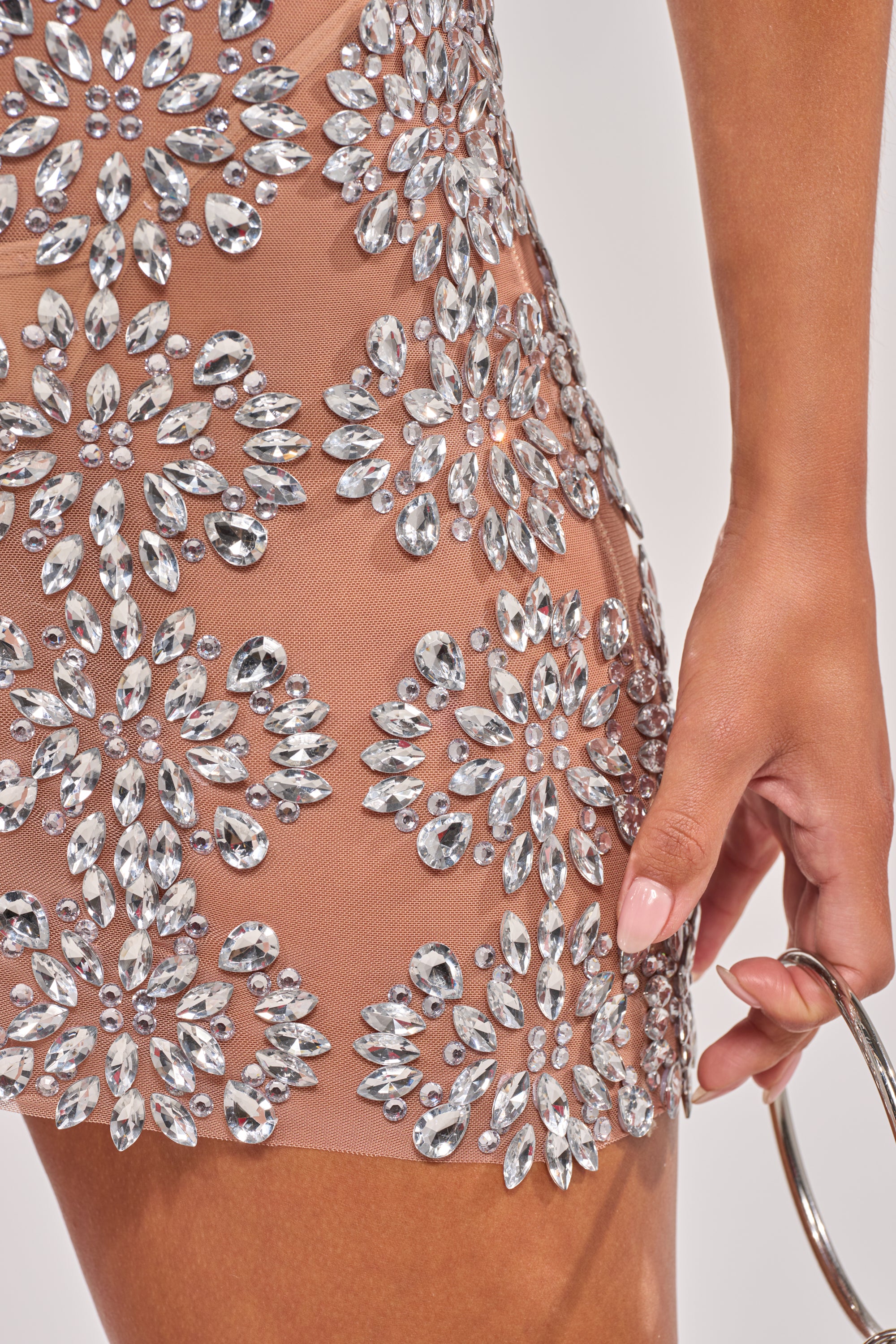 Close-up of a person wearing the SO TEMPTING RHINESTONE OFF SHOULDER MINI DRESS, featuring dazzling crystal floral patterns, and holding a metallic circular handle purse. 8