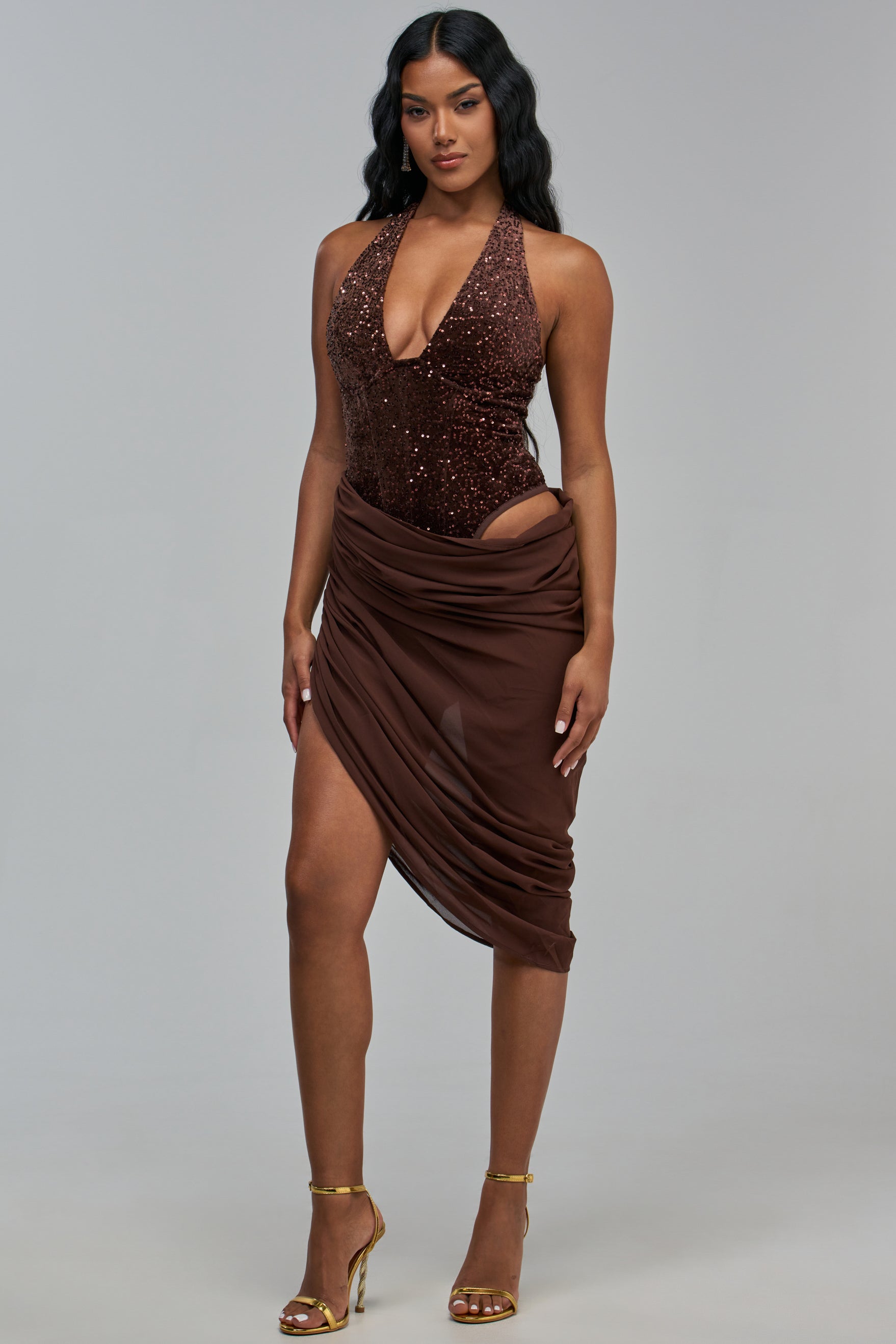 A woman wears the WILD SIDE VELVET MIDI DRESS, a brown sequined halter bodysuit with a matching draped midi skirt, styled with gold high-heeled sandals.