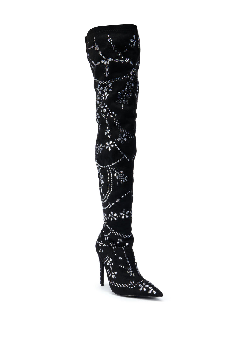 The AZALEA WANG AGELESS STILETTO BOOT IN BLACK SUEDE is a striking tall footwear piece, crafted with black suede and decorated with intricate white patterns and sparkling embellishments. It features a rhinestone stiletto heel and a pointed toe, elegantly displayed against a plain white background.