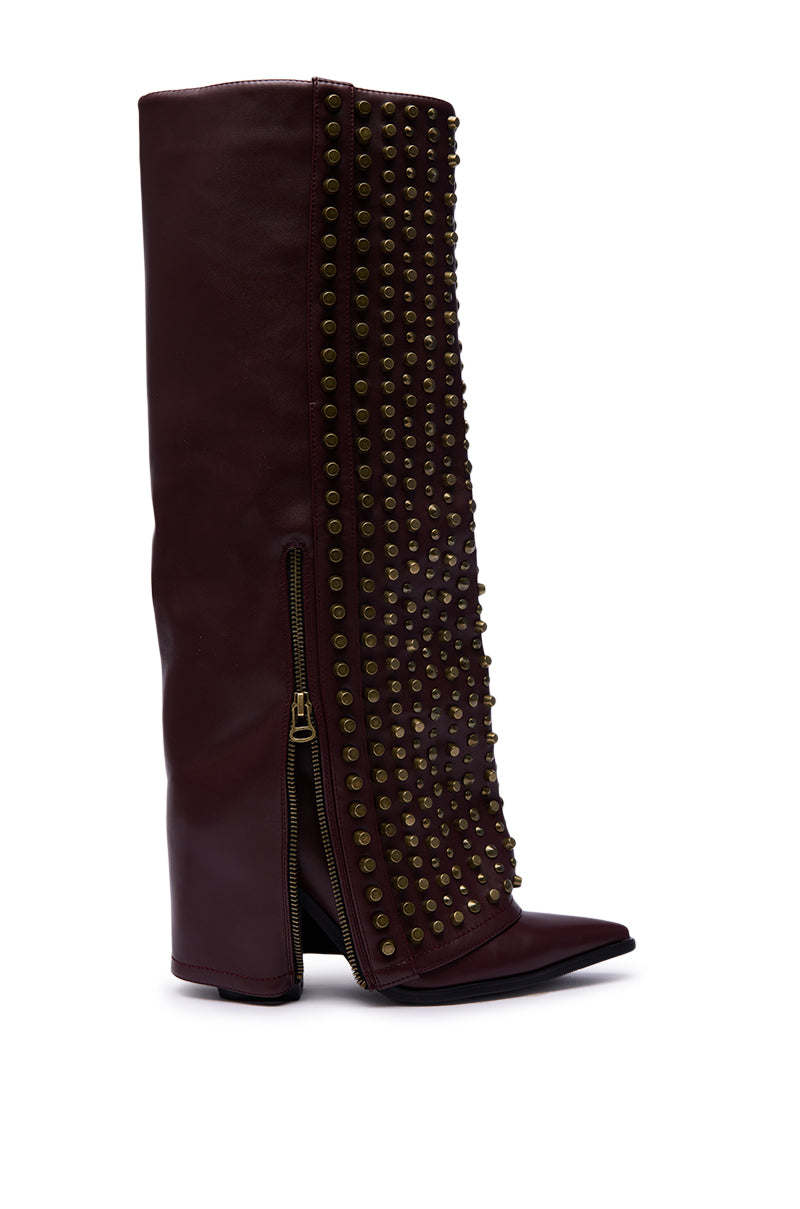 The AZALEA WANG AGUSTUE BURGUNDY STUDDED WESTERN BOOT is a tall, knee-high western boot with a pointed toe, side zipper, slouched shaft, high heel, and front panel detailed with rows of brass studs.
